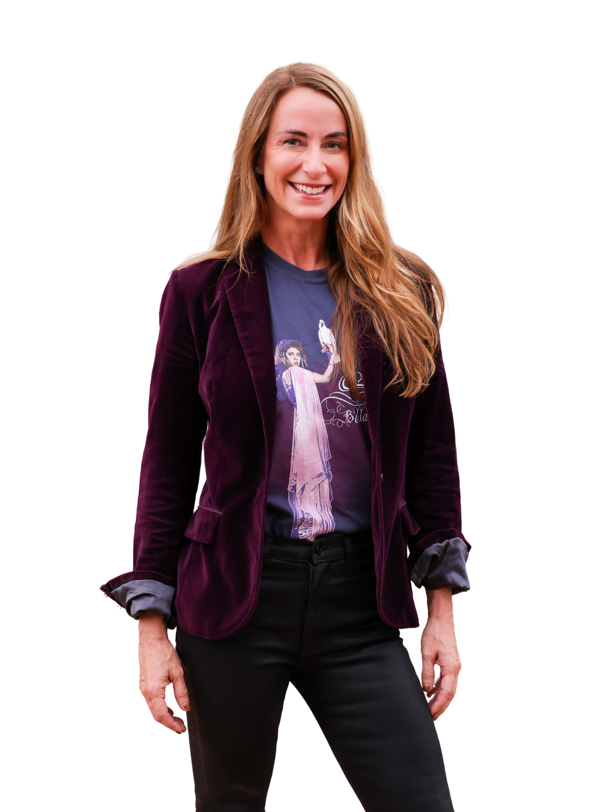 A woman with long, wavy, light brown hair smiling, wearing a purple velvet blazer over a graphic T-shirt, with black pants.
